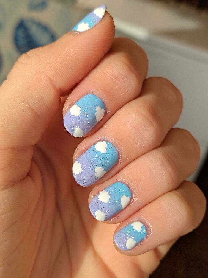Nail art featuring a gradient blue sky design with white clouds on a person's fingernails.