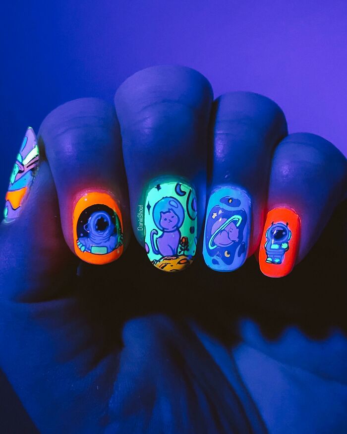 Neon nail art featuring space and cat designs glowing brightly under blacklight for creative nail art ideas.