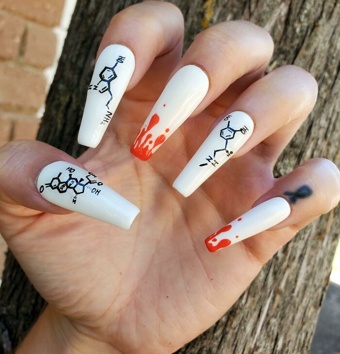 Long white nails with chemical structure nail art designs and red paint drip accents on a natural hand outdoors.