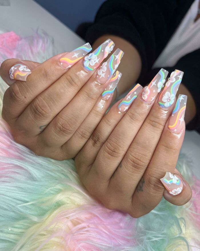 Long nails with nail art featuring colorful swirls and 3D white flower designs on a pastel background.