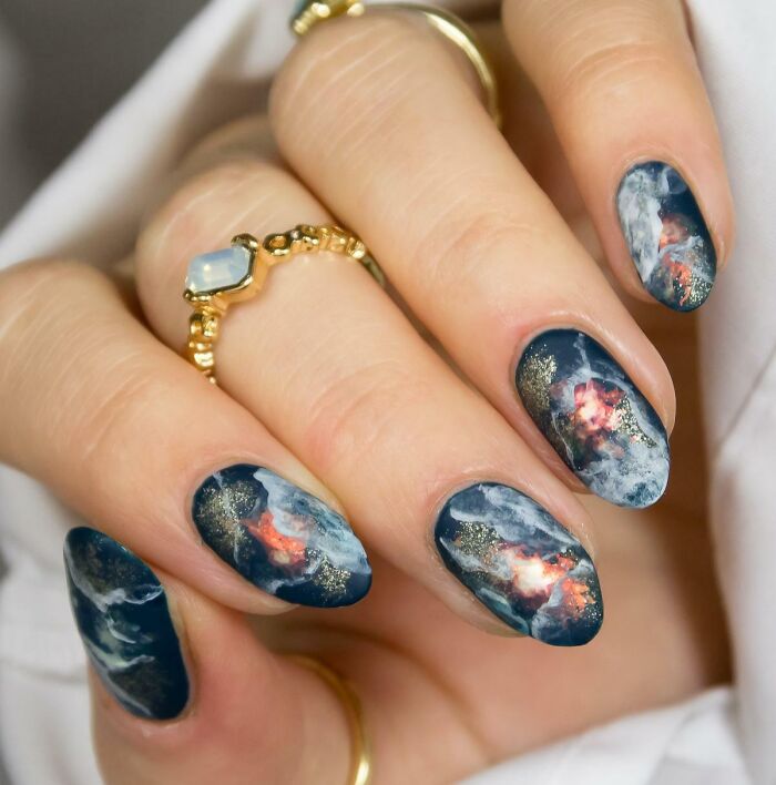 Nails with detailed nail art design featuring dark blue, white, orange, and gold accents in an artistic pattern.