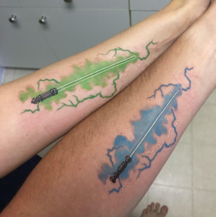 Two arms with matching brother and sister lightsaber tattoos in green and blue, symbolizing sibling connection.
