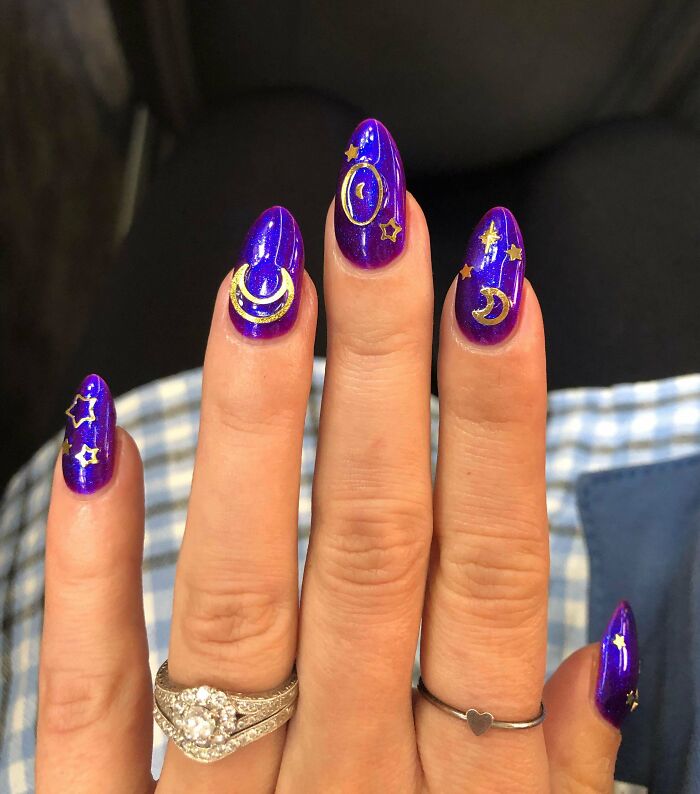 Blue and gold celestial nail art featuring stars and moons on a hand with rings.