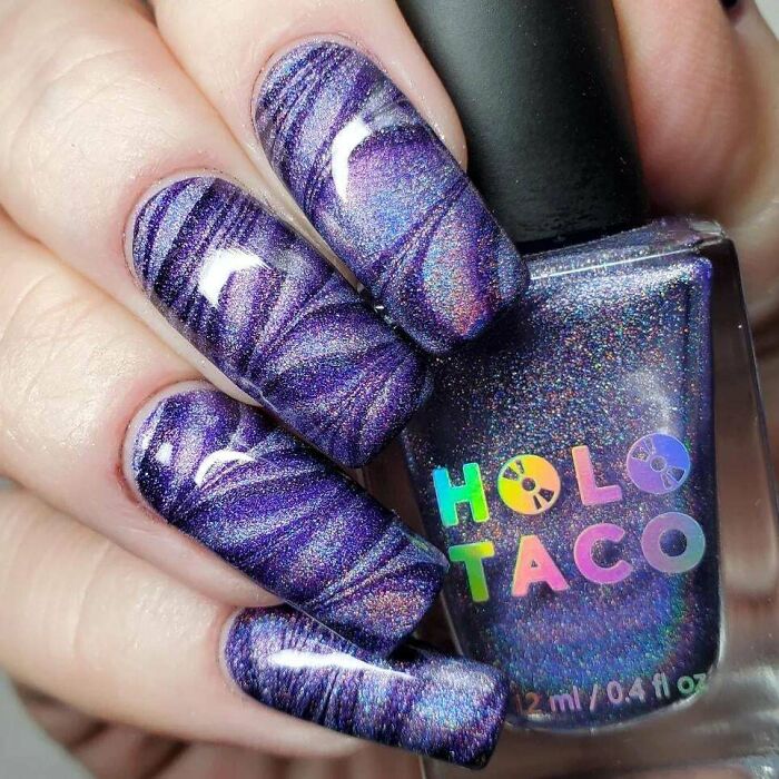 Purple holographic nail art design with swirling patterns.