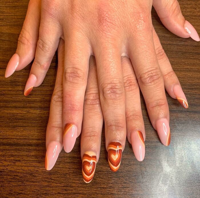 Hands with almond-shaped nails featuring pink and brown swirled nail art designs on a wooden surface, showcasing nail art ideas.
