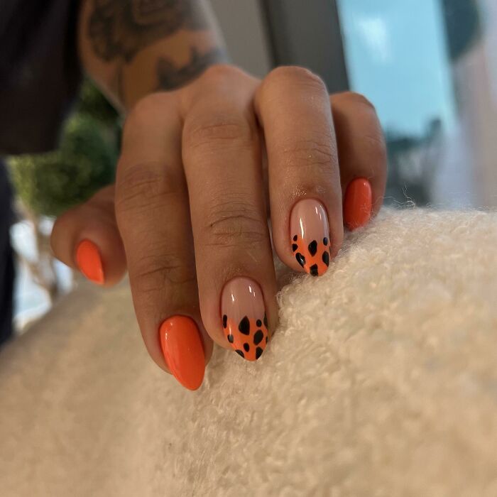 Hand with orange and black nail art design featuring leopard print details, showcasing creative nail art ideas and stylish manicures.
