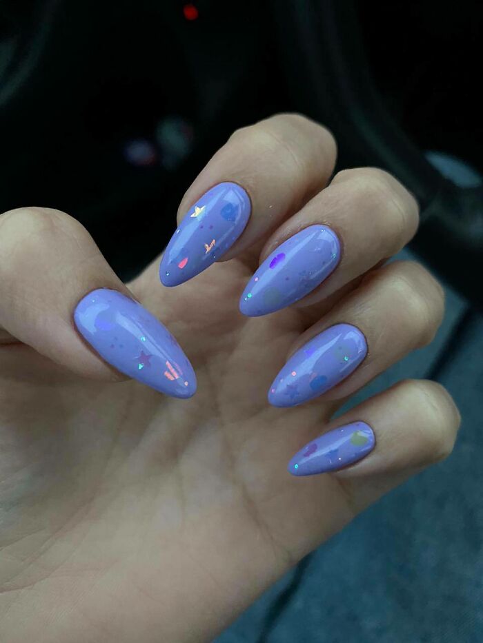 Purple nail art with glossy finish and small colorful accents on a person's hand.