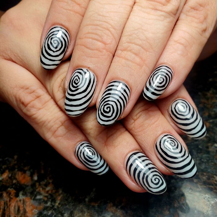 Black and white spiral nail art design on manicured hands.