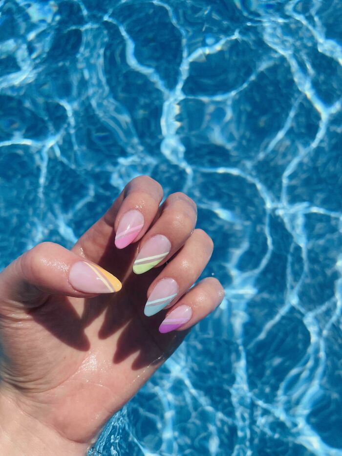 Colorful nail art with pastel stripes, perfect for your next appointment, set against a shimmering blue pool background.