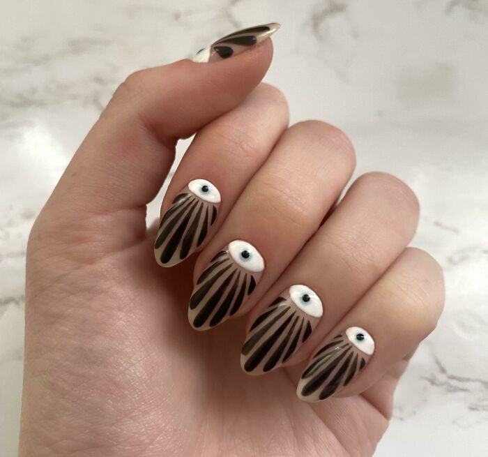 Creative nail art featuring black and white designs with eye motifs on manicured nails.
