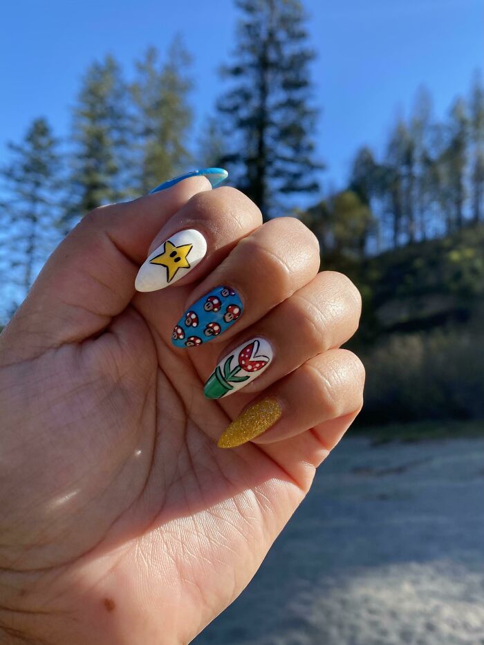 Hand with colorful nail art designs including a yellow star, mushrooms, flower, and glitter, showcasing creative nail art ideas.
