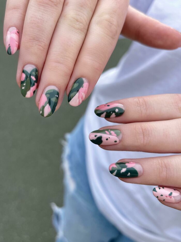 Close-up of hands showing nail art ideas featuring pink and green abstract designs on medium-length nails.