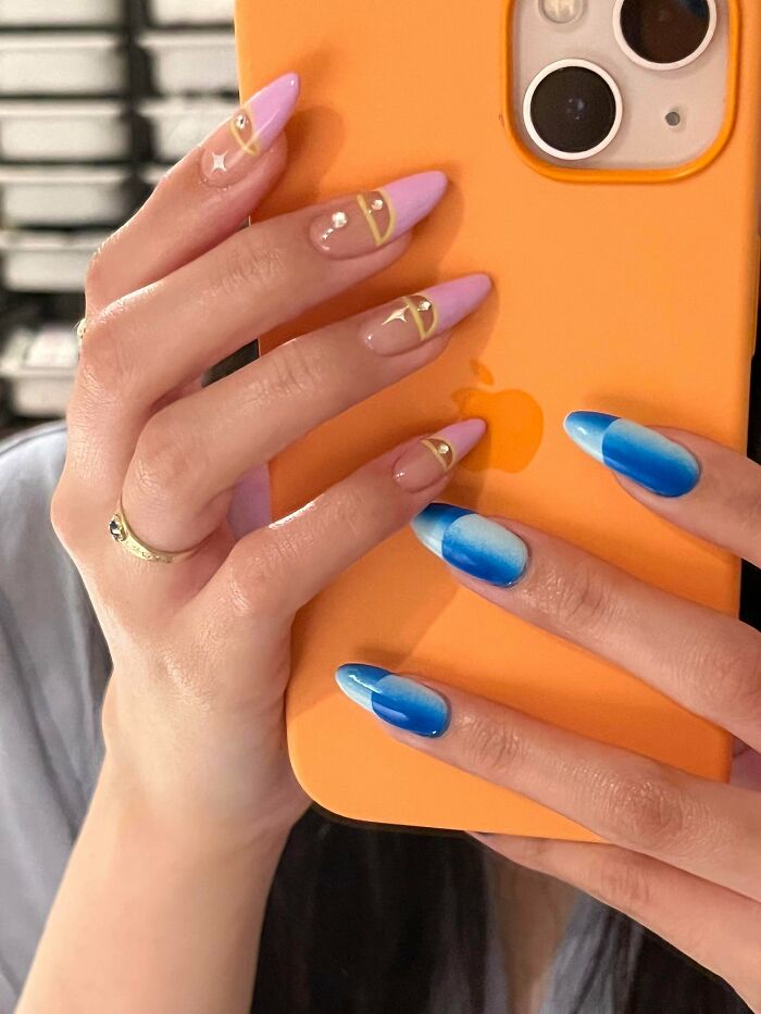 Hands holding an orange phone case with nail art ideas featuring purple tips with gold accents and blue gradient designs.