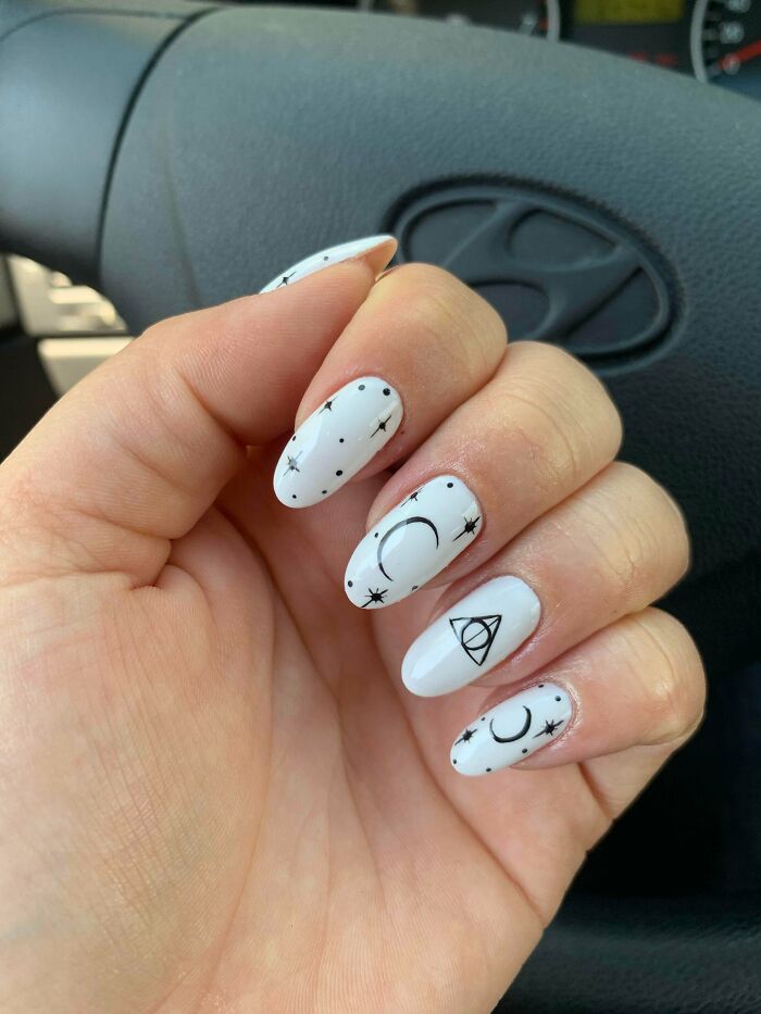 White nails with black celestial and geometric designs, showcasing creative nail art ideas for unique tiny artworks.