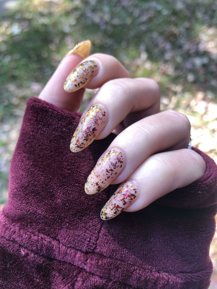 Decorative nail art with gold flakes on long nails, perfect for your next appointment.
