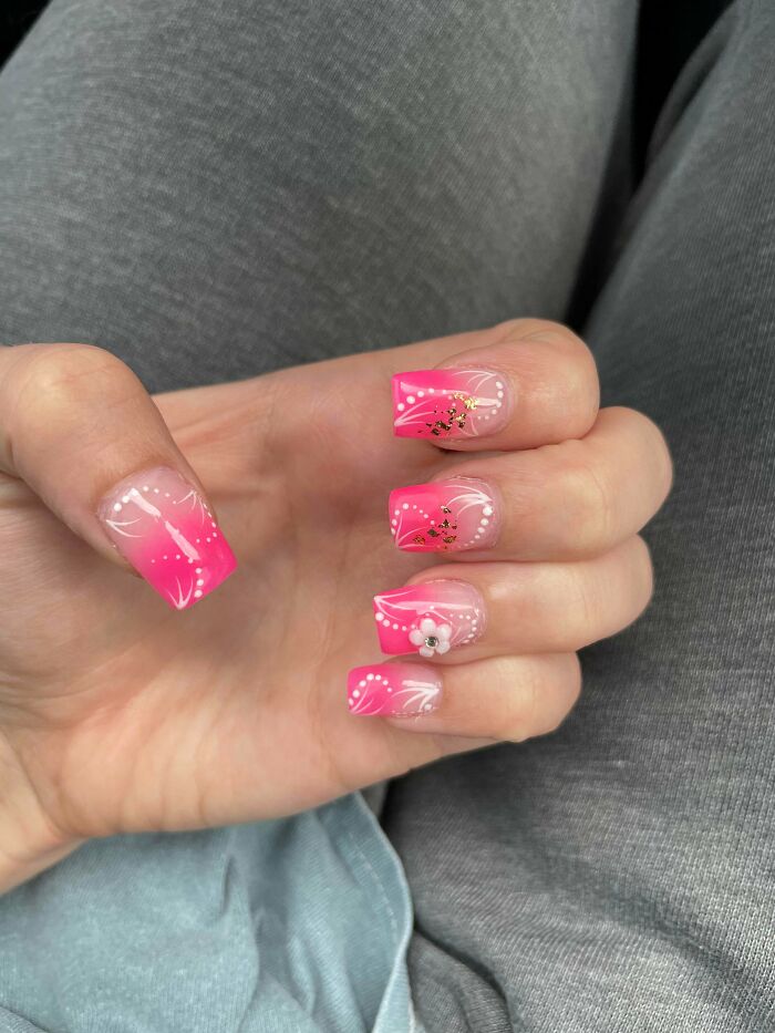 Pink nail art ideas with white swirls, dots, gold foil accents, and a small flower embellishment on square-shaped nails.