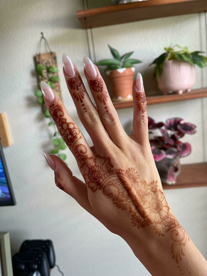 Hand with long almond-shaped nails and intricate henna designs, showcasing creative nail art ideas for elegant nail decoration.