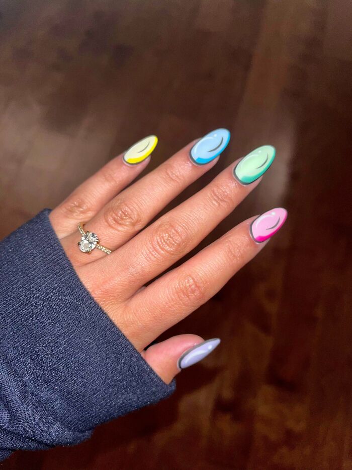 Hand with colorful nail art ideas featuring pastel hues and black line designs, wearing a ring on a dark background.