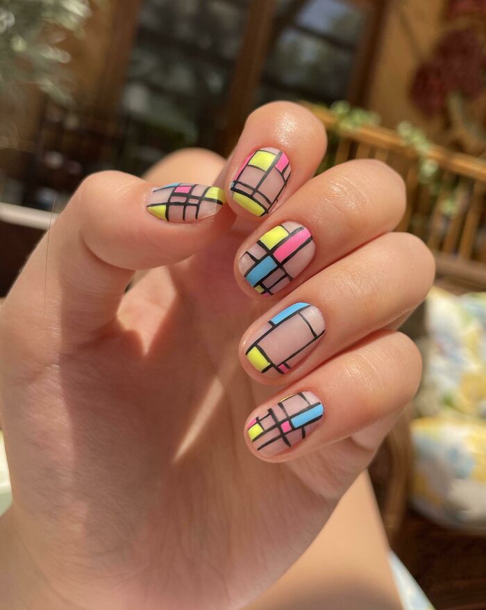 Hand with colorful geometric nail art design featuring pastel yellow, pink, and blue shades, showcasing creative nail art ideas.