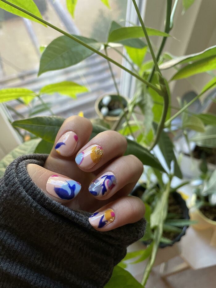 Hand with colorful abstract nail art designs featuring blue, pink, and gold accents, showcasing creative nail art ideas.