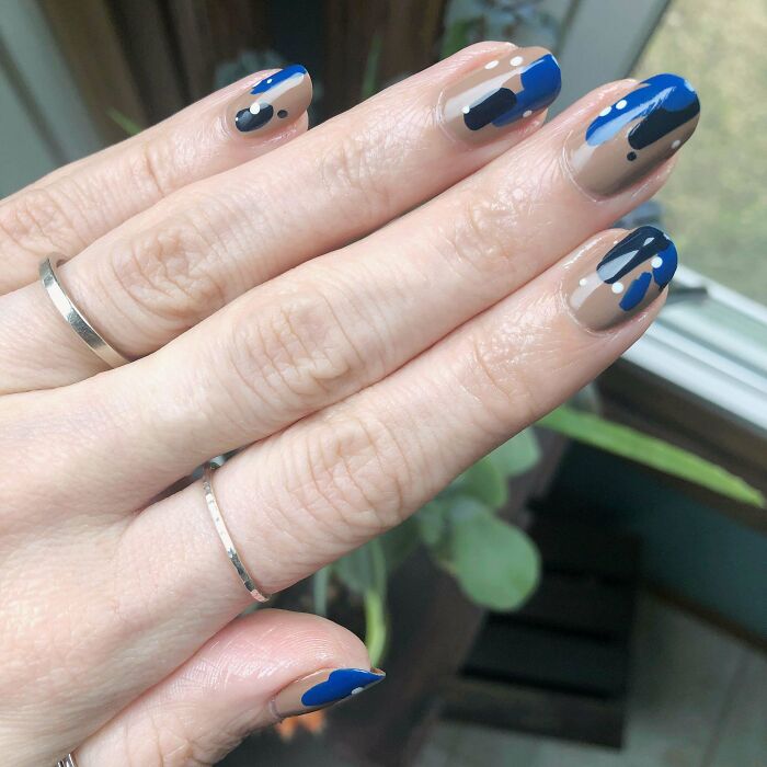 Hand with blue and black abstract nail art designs on n**e base, showcasing creative nail art ideas for stylish manicures.