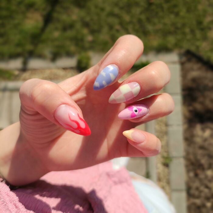 A hand displaying colorful nail art ideas with a mix of patterns and designs, outdoors.
