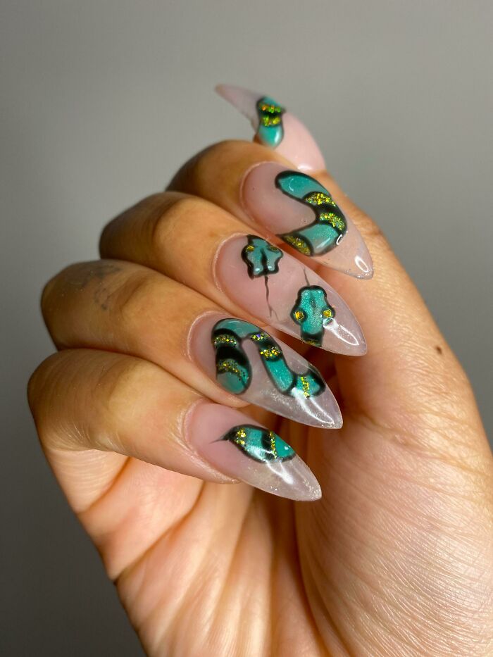Nail art featuring green and gold abstract designs on long acrylic nails.