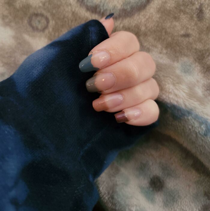 Close-up of a hand with trendy nail art featuring mixed matte and glossy finishes on a cozy textured background.