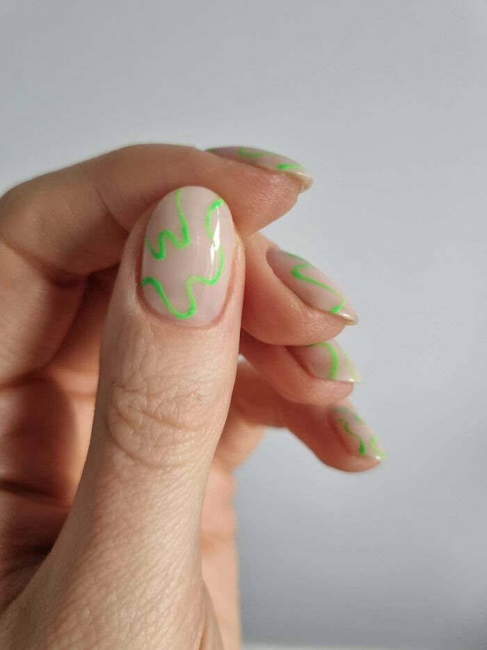 Hand showing nails with minimalistic nail art ideas featuring neon green abstract lines on a natural base color.