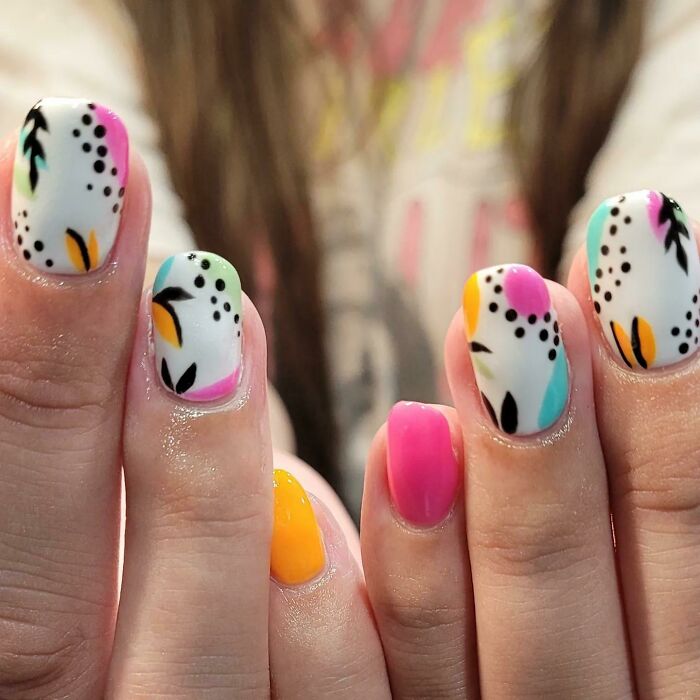 Colorful nail art with abstract patterns in pink, yellow, and green on white background.