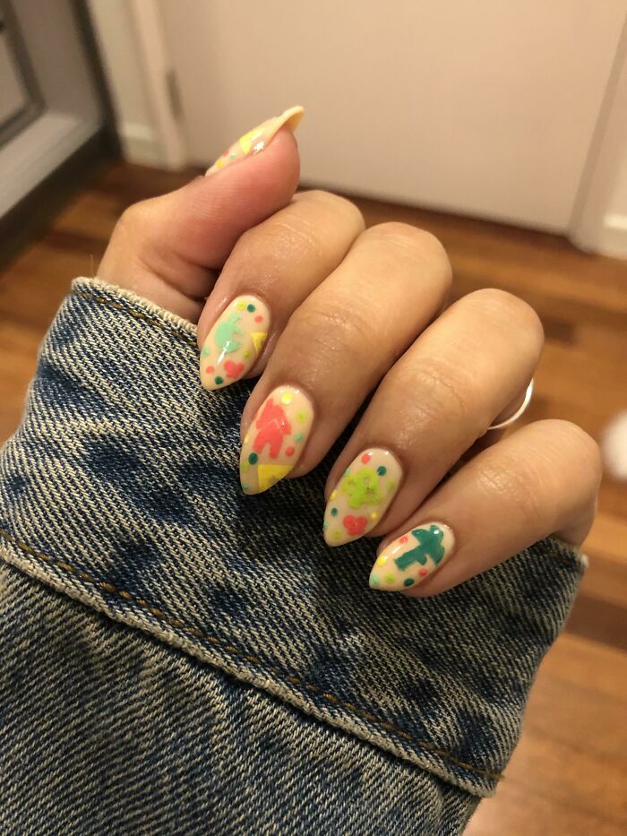 Colorful nail art with abstract shapes and dots on a hand wearing a denim jacket.