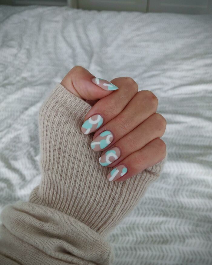 Hand with pastel blue and white abstract nail art designs, showcasing creative nail art ideas on a cozy beige sweater background.