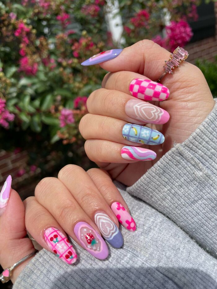Colorful nail art ideas featuring hearts, cherries, flowers, and geometric designs on long, almond-shaped nails outdoors.