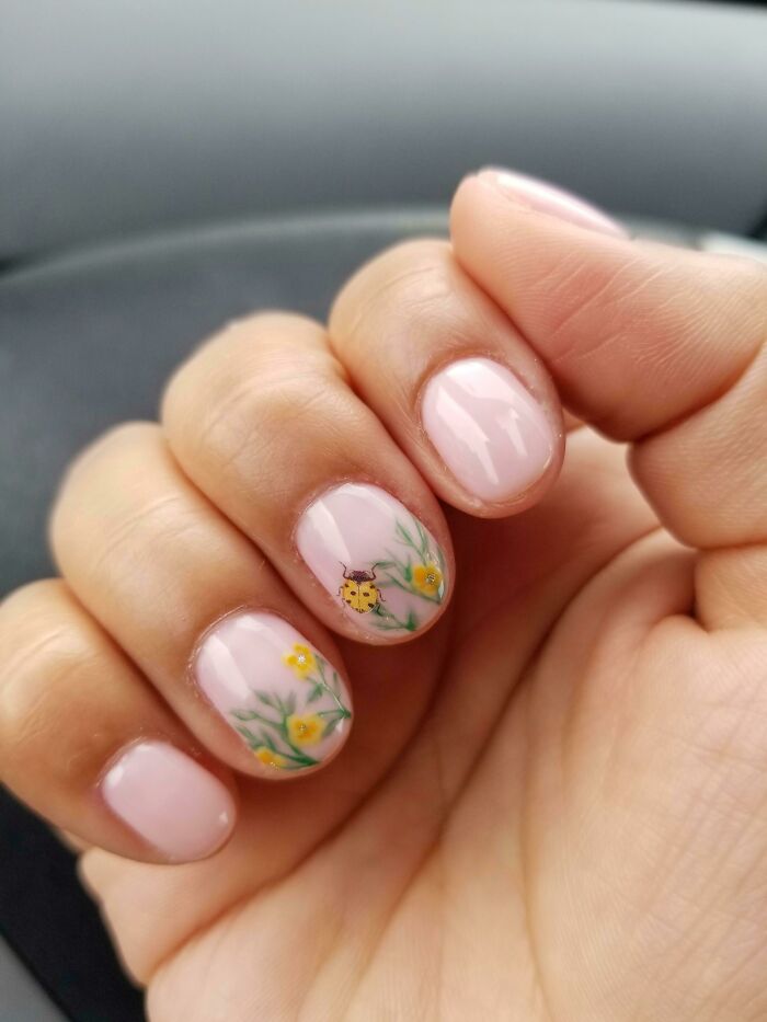 Close-up of nails with pink nail art featuring delicate yellow flowers and a small ladybug design on a hand.