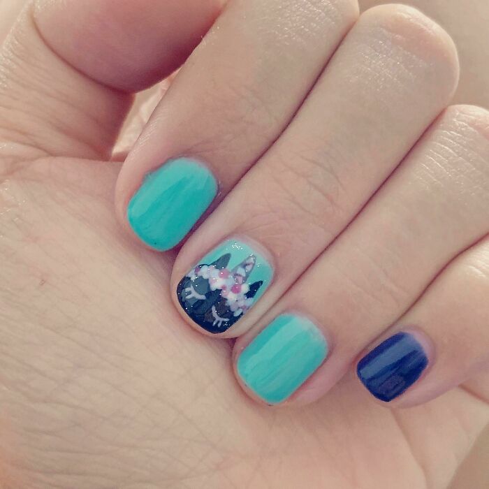 Close-up of nails featuring turquoise polish and a detailed unicorn design as part of creative nail art ideas.