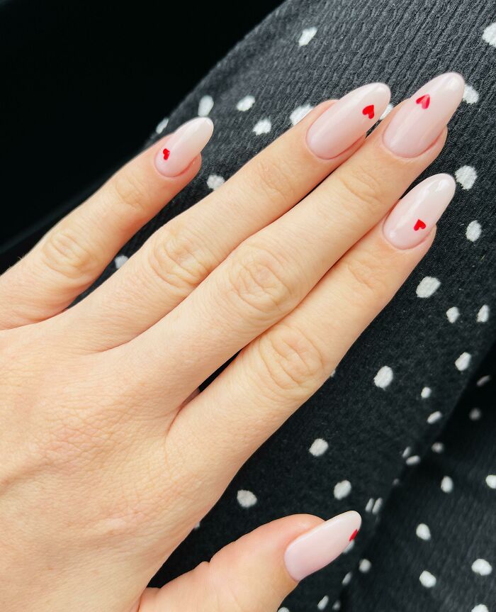 Stylish nail art with small red heart designs on natural-toned nails.