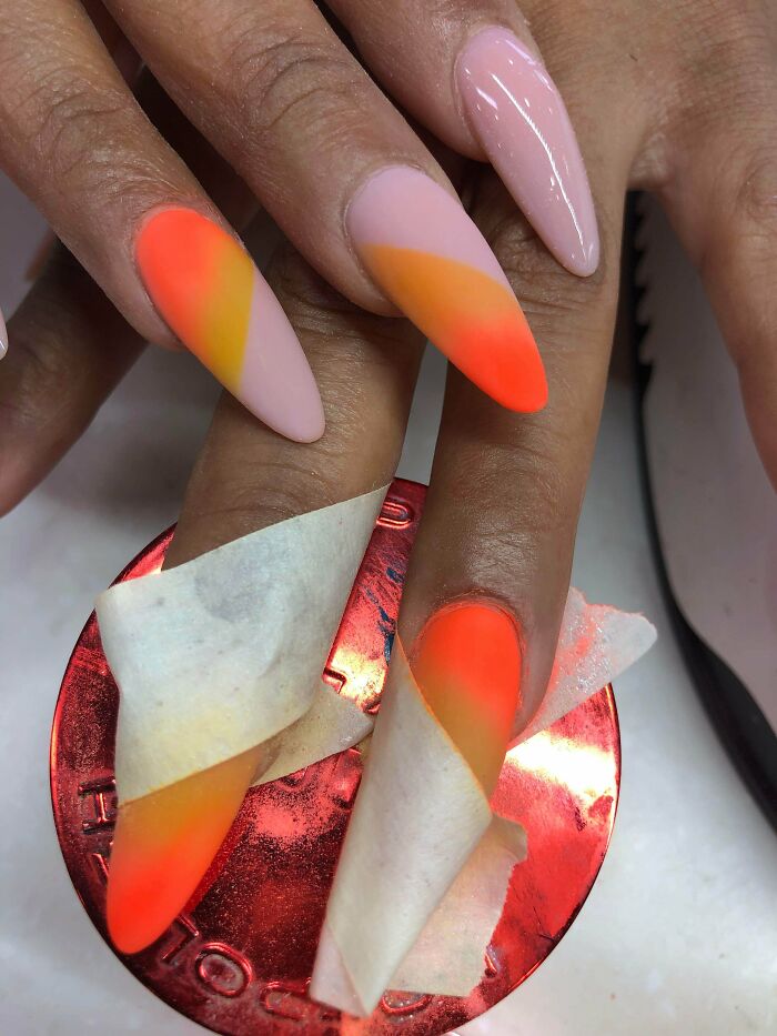 Close-up of hands with vibrant neon orange and yellow gradient nails, showcasing creative nail art ideas for stylish manicures.
