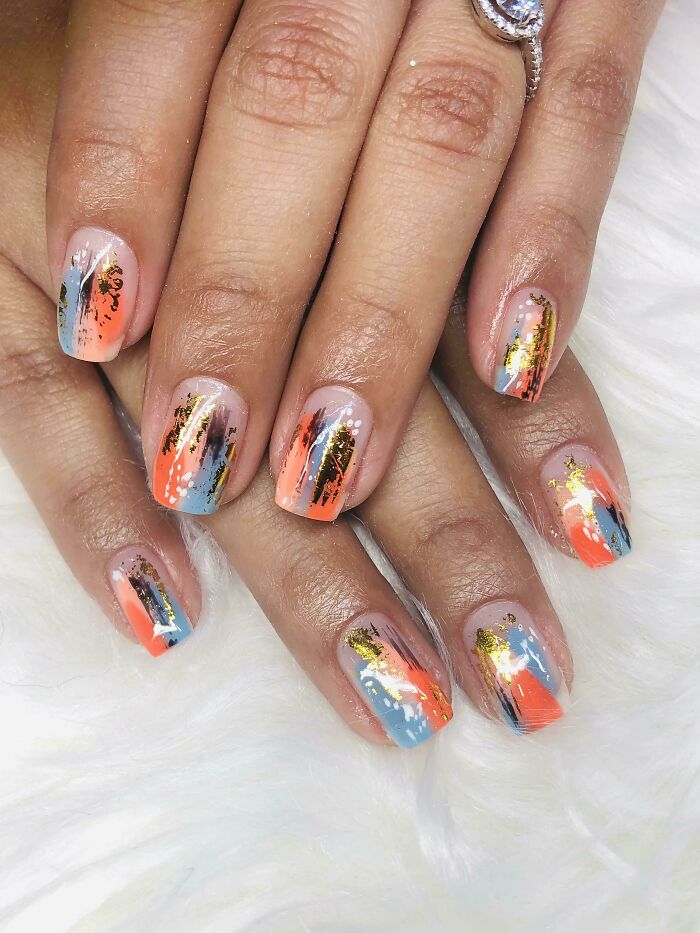 Nail art ideas featuring abstract brush strokes in coral, blue, and gold foil on short, natural nails.