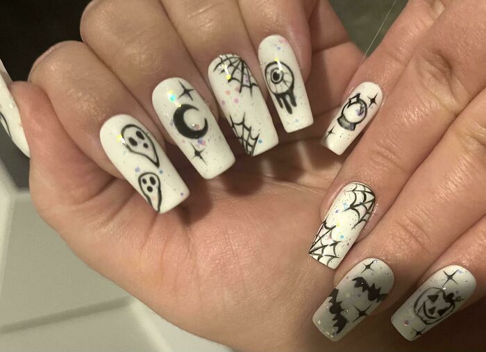 White Halloween-themed nail art featuring ghosts, spider webs, bats, and spooky symbols in black details.