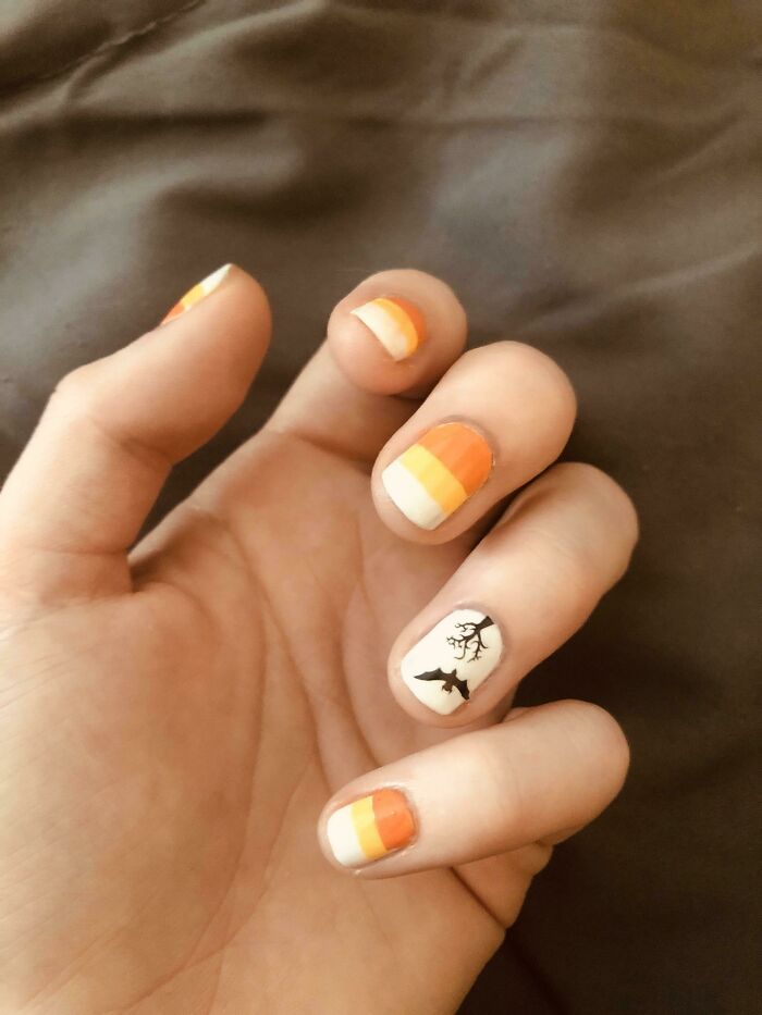 Halloween-inspired nail art with orange, white, and black accents featuring bats and trees.