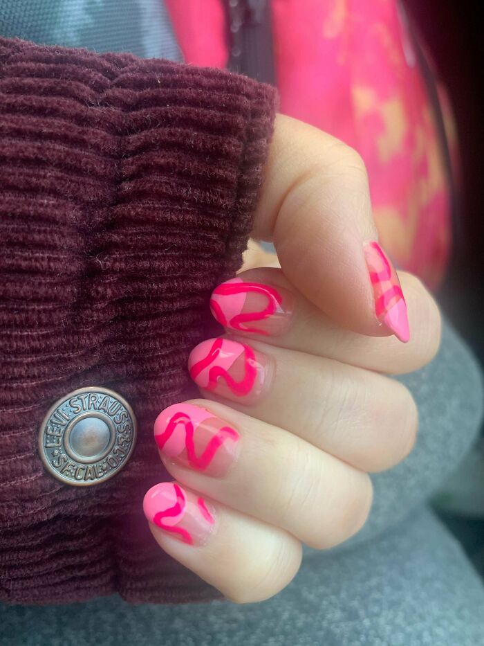 Pink and clear wavy nail art design on short nails, accented by a burgundy sleeve.