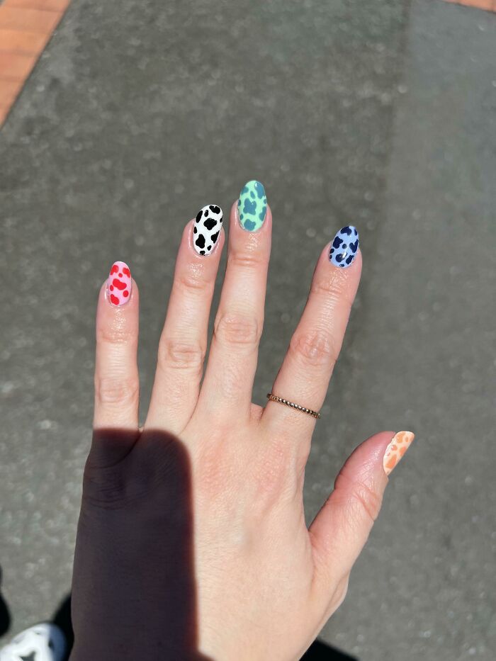 Colorful leopard print nail art on a hand with a thin gold ring.