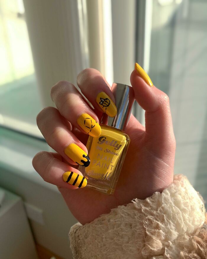 Hand holding yellow nail paint with bee-inspired nail art designs, showcasing creative nail art ideas.