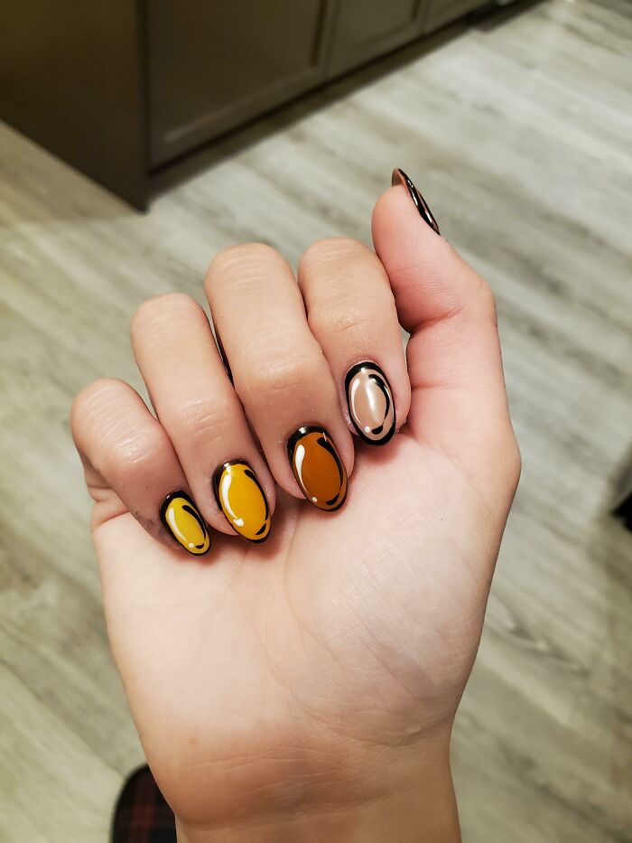Close-up of a hand with trendy nail art featuring glossy brown and orange designs.