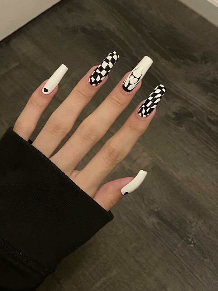 Hand with black and white nail art ideas featuring checkerboard and heart designs on long square nails.