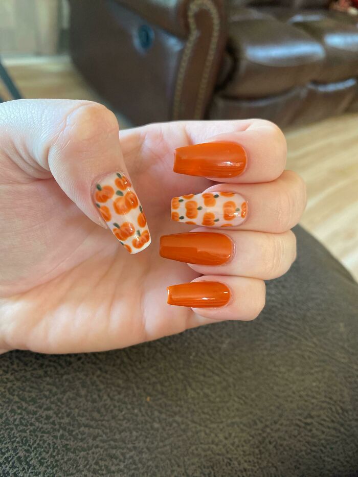 Hand with orange nail art, featuring solid glossy nails and pumpkin designs on two nails for creative nail art ideas.