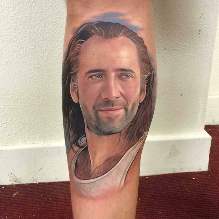 Quality tattoo of a man's face on a person's calf with long hair and a serene expression.