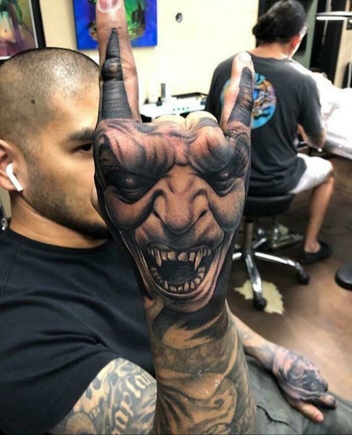 A man displays an intricate tattoo design of a snarling face on his hand.