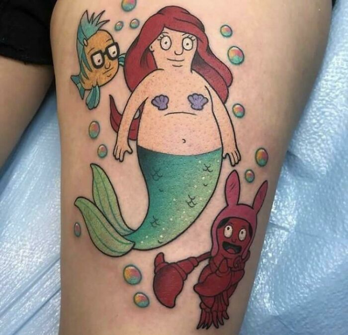 Cartoon-style tattoo featuring a mermaid and sea creatures, highlighting a humorous design concept.