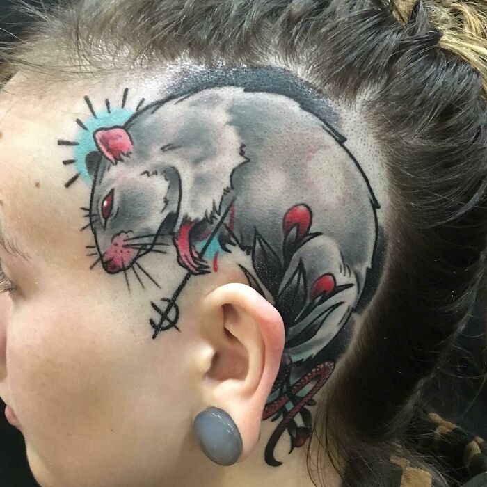 A detailed rat tattoo on a person's shaved scalp with vibrant colors and intricate design.